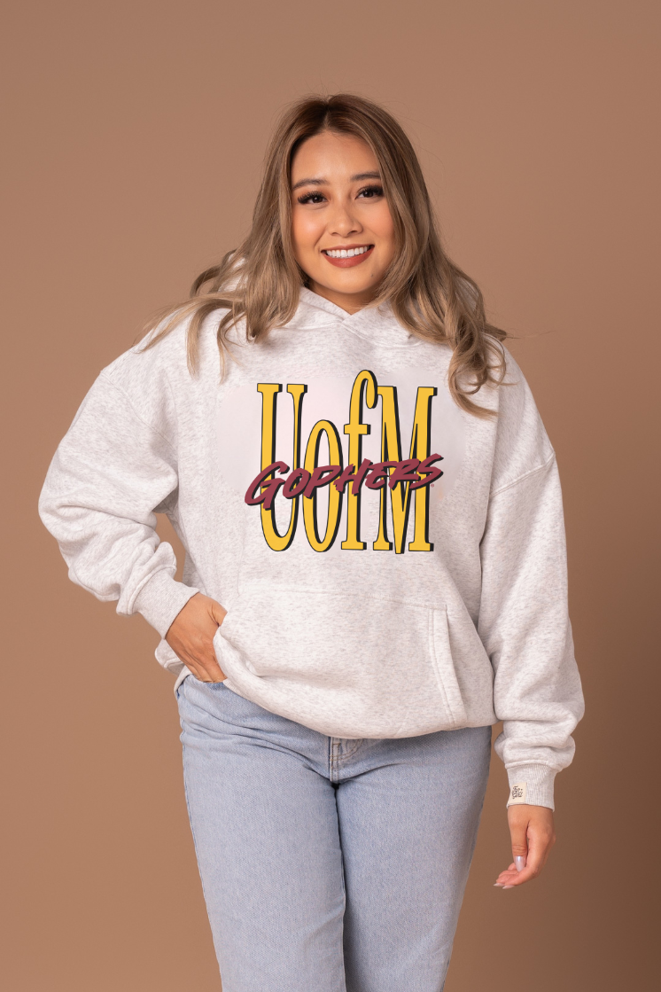 Woman wearing a heather grey hoodie with 'U of M Gophers' text in yellow and maroon