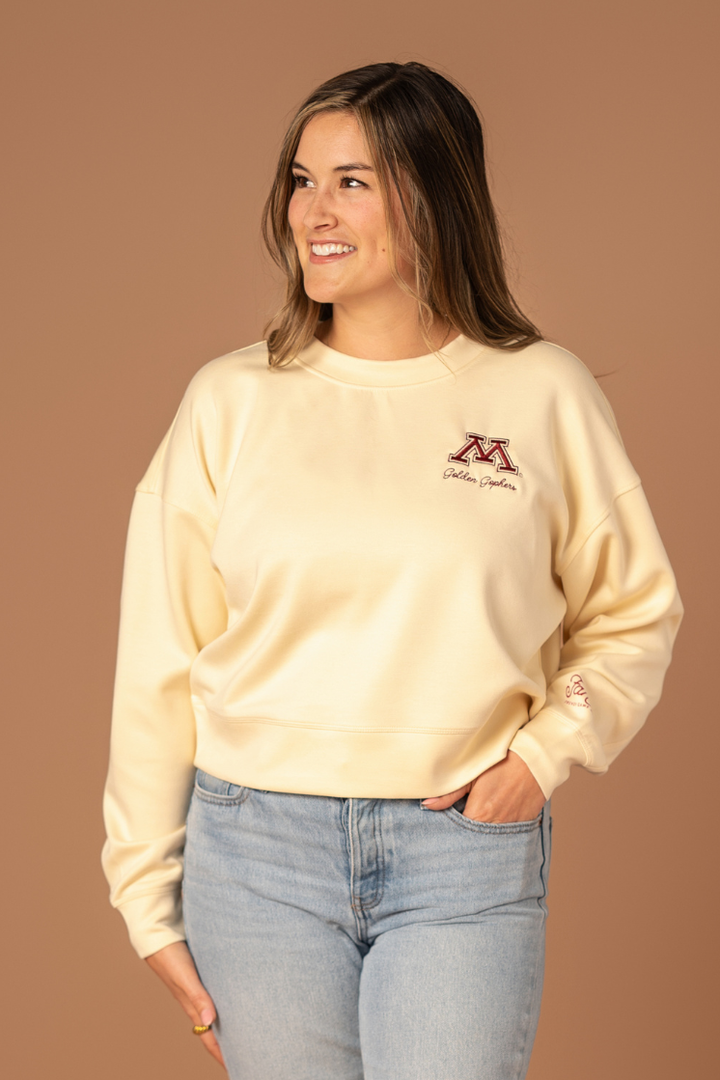 close up image of a girl wearing a bone colored supersoft crewneck with a M logo and Golden Gophers embroidered in maroon on the left side pocket of the crew