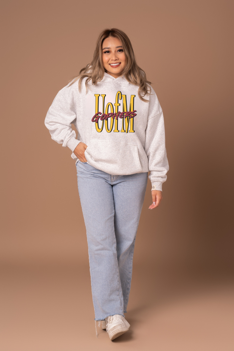 Woman wearing a heather grey hoodie with 'U of M Gophers' text in yellow and maroon