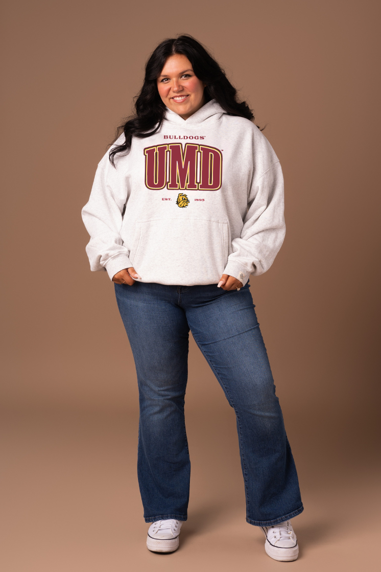 Woman wearing a grey hoodie with 'Bulldogs' and 'UMD' text in maroon with a gold outline