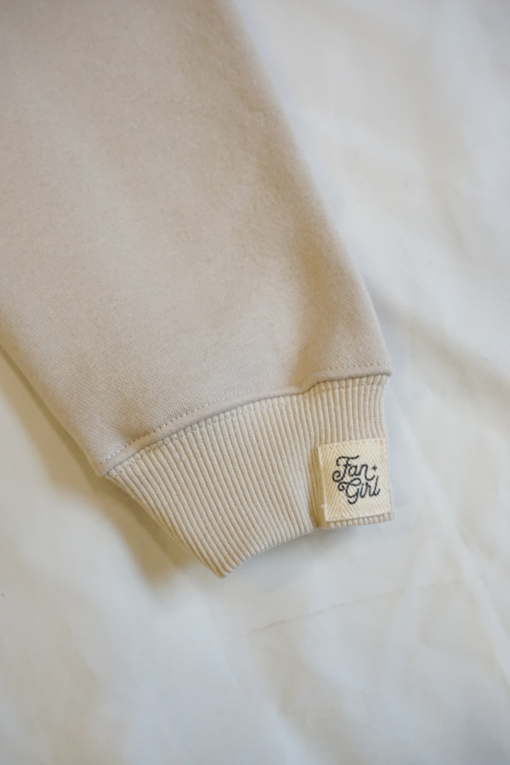 Close-up of a beige sweater with a brand label on a light background