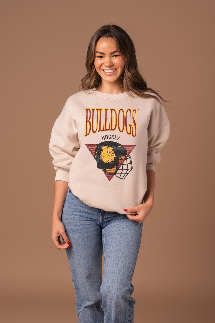 Close up picture of a girl wearing a beige sweatshirt with 'Bulldogs Hockey' design on a brown background