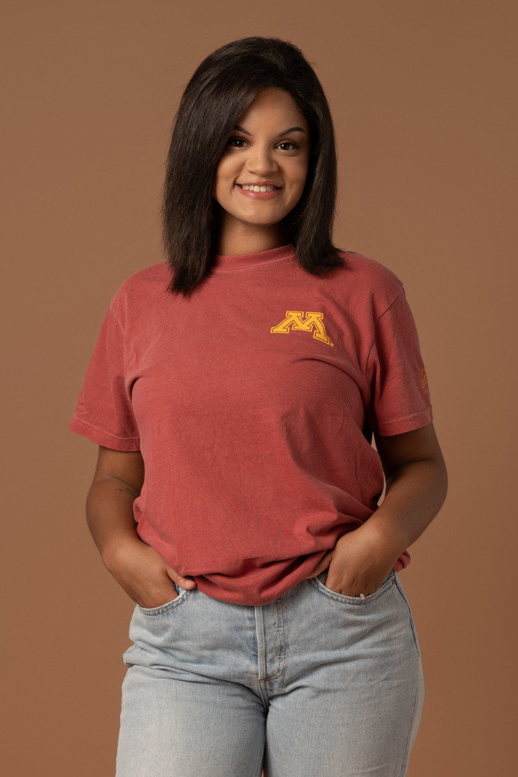 close up image of girl wearing a crimson colored t-shirt with a gold M screenprinted on the left pocketside of the tee