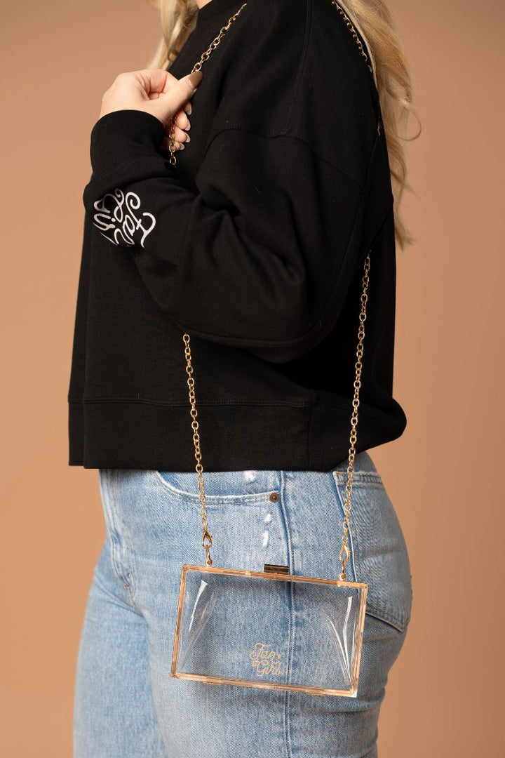 picture of girl's side profile with a clear square shaped purse on her shoulder with gold detail and a small gold Fan Girl logo on the front 